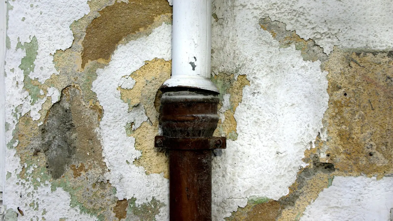 Peeling, stained wall around a rusted pipe